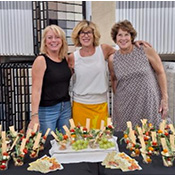 Carolyn Manhatton of Excelsior Paint and Design standing with other women; behind them is a carpet display and in front is food offered at the meet and greet.